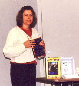 Karen Joy Fowler presenting the books she has written.  She is holding her newest book, BLACK GLASS.  SARAH CANARY and SWEETHEART SEASON are displayed upon the table.
